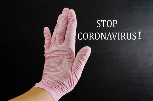 χέρι σε ένα ιατρικό γάντι δείχνει στάση χειρονομία. Μαύρο φόντο. Η επιγραφή σταματά coronavirus. - Φωτογραφία, εικόνα
