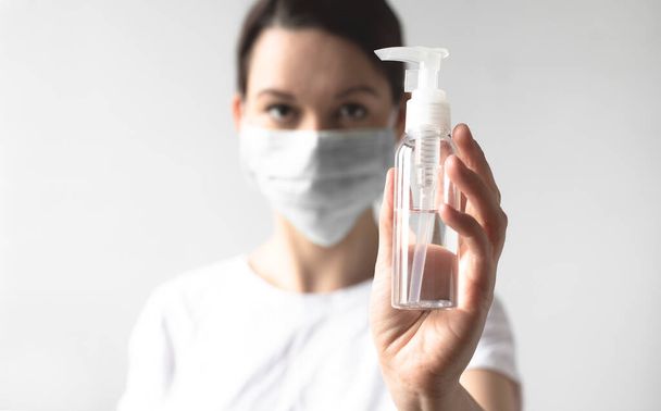 Coronavirus concept. Girl wearing a protective medical mask holding a bottle with a sanitizer. Hygiene during a pandemic covid-19 virus protection. Protect your health - Фото, изображение