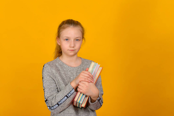 Dívka s učebnicemi v ruce stojí na žlutém pozadí - Fotografie, Obrázek