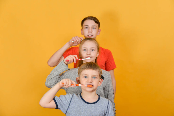Τα παιδιά κρατούν μια οδοντόβουρτσα στα χέρια τους και στέκονται στη σειρά σε κίτρινο φόντο. - Φωτογραφία, εικόνα