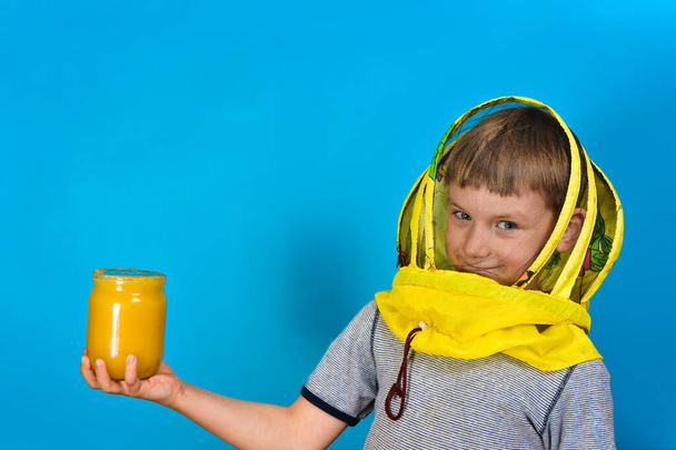 蜂から保護マスクの男の子は青い背景に蜂蜜の瓶を手に持っています. - 写真・画像