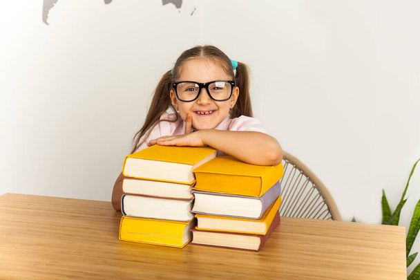 Ευτυχισμένο κοριτσάκι με πολύ βιβλίο στο γραφείο. Απομονωμένα σε λευκό φόντο - Φωτογραφία, εικόνα