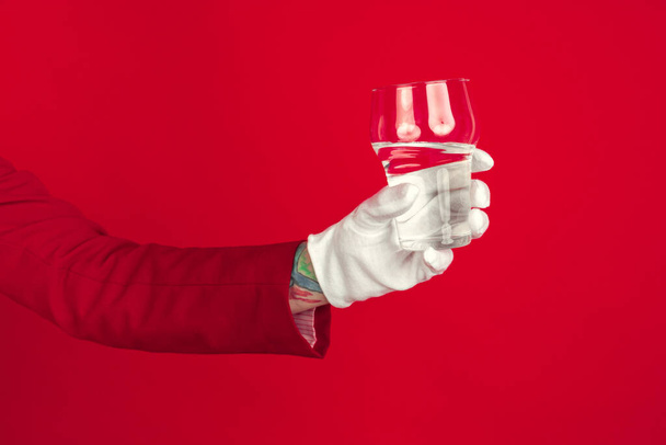 Mano femenina en guante blanco sosteniendo vaso de agua pura sobre fondo rojo
 - Foto, Imagen