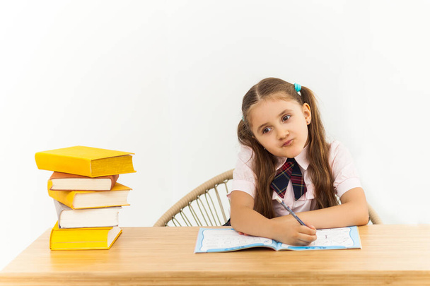 Una niña feliz con mucho libro en el escritorio escribiendo algo en copybook. Home Concepto de aprendizaje
 - Foto, imagen