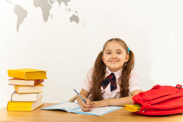 Happy little girl with a lot of book at the desk writing something in copybook. Home Learning Concept - Photo, Image