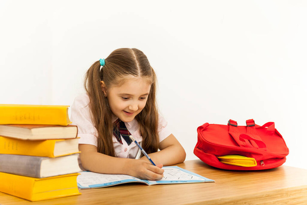 Glückliches kleines Mädchen mit vielen Büchern am Schreibtisch, die etwas in ein Copybook schreiben. Home Learning Konzept - Foto, Bild