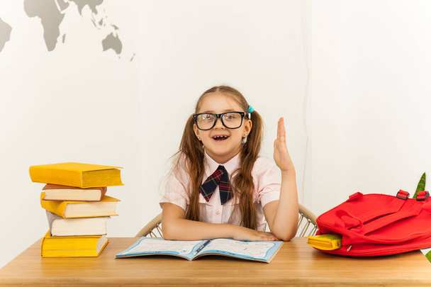 Щаслива студентка-дівчинка в окулярах з відкритим блокнотом тягне за собою руку за столом у класі. Концепція освіти
 - Фото, зображення