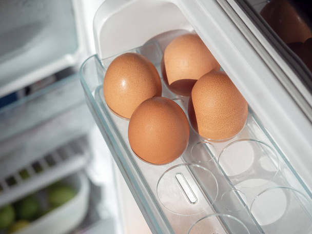 Four fresh chicken eggs on shelf of white refrigerator, top view. - Фото, изображение