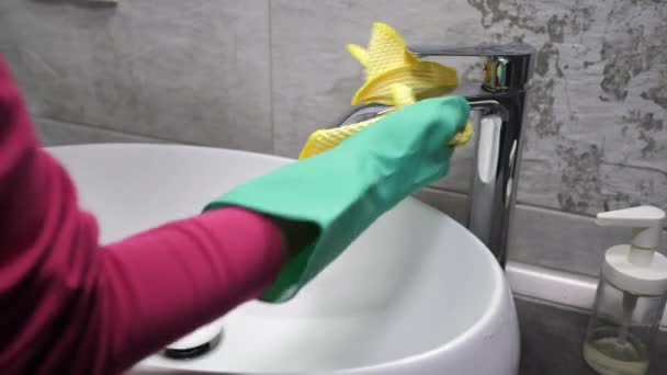 女性は黄色い布で流しを洗う。コロナウイルス流行発生。水のタップを消毒するためにぬれたワイプを使用して保護手袋の手のクローズアップ - 映像、動画