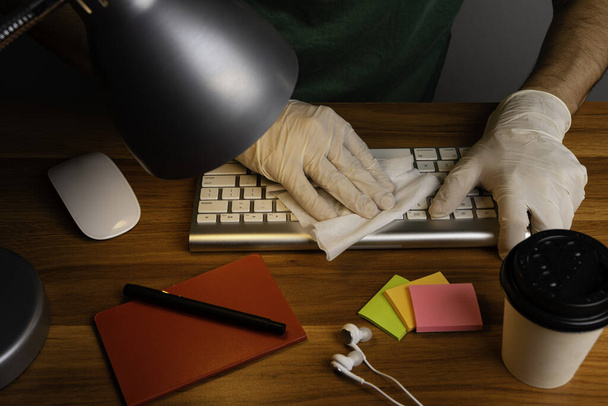 Людина з захисними рукавичками на робочому місці, що виконує гігієну клавіатури
. - Фото, зображення