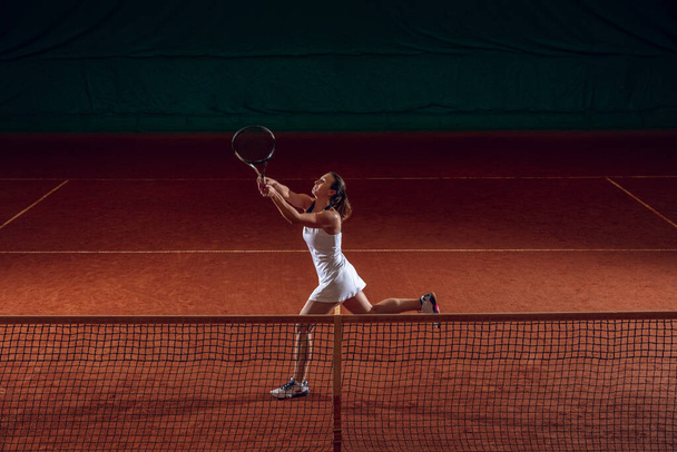 Young caucasian professional sportswoman playing tennis on sport court background - Foto, afbeelding