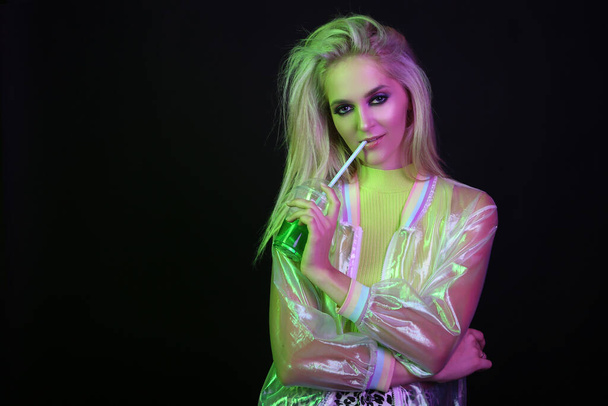 Sexy blonde Frau in Neonlicht in einem Nachtclub. Mit einem Glas grünen Getränks, Cocktails, Alkohol. Nachtleben. Neunziger Jahre. - Foto, Bild