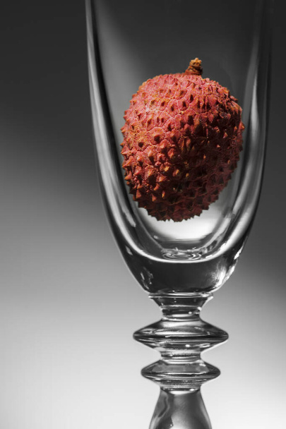 A parte superior de uma taça de champanhe curva preenchida com uma fruta de lichia vermelha contra um gradiente claro-escuro
. - Foto, Imagem