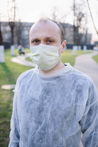 Sarı koruyucu maske takmış genç bir adamın portresi ve caddede tıbbi elbise. 2020 pandemik koronavirüs. Karantina. Virüs konsepti. Salgın hastalık. - Fotoğraf, Görsel