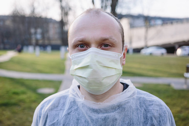 Szoros portré egy fiatalemberről sárga védőmaszkban és orvosi köpenyben az utcán. Pandémiás koronavírus 2020. Karantén. Vírus koncepció. Járványos fertőzés. - Fotó, kép