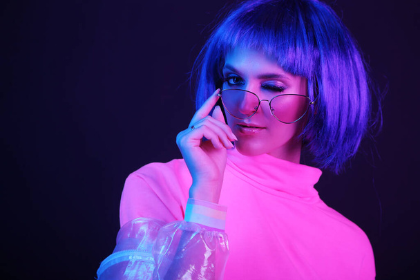 Neon light studio close-up portrait of happy woman model in a wig in sunglasses. Nightlife, party in a nightclub. Copy space. - Фото, изображение