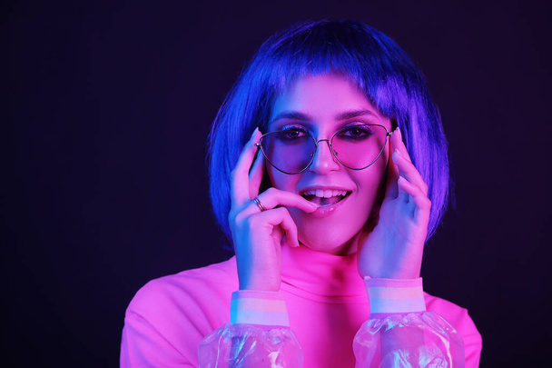 Neon light studio close-up portrait of happy woman model in a wig in sunglasses. Nightlife, party in a nightclub. Copy space. - Foto, Bild