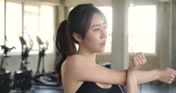 Attractive woman doing stretch in the gym. Young beautiful asian woman stretching hands for warm up before sport workout. Slow motion. Healthcare, Exercise and Sport concept. - 映像、動画
