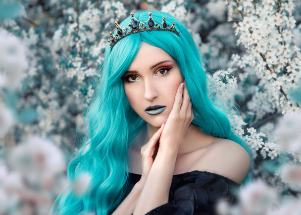 Portrait of young queen with blue hair  posing on blooming tree background - Фото, изображение