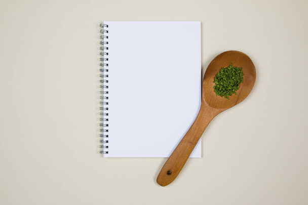 Ξύλινη κουτάλα με λίγο μπαχαρικό βότανο και ένα κενό σημειωματάριο σελίδα - Φωτογραφία, εικόνα