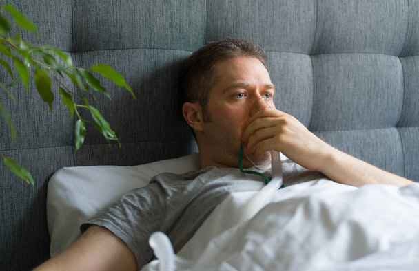 Sairas mies, jolla on hengityssuojain naamassa sängyssä. Koronaviruksen ennaltaehkäisyn käsite. - Valokuva, kuva
