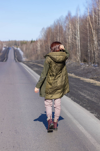 A young woman walks by the side of the road. Road in the forest - Foto, Imagem