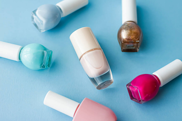 Garrafas coloridas de esmalte de unhas em fundo azul, maquiagem orgânica e produtos cosméticos para a marca de beleza
 - Foto, Imagem