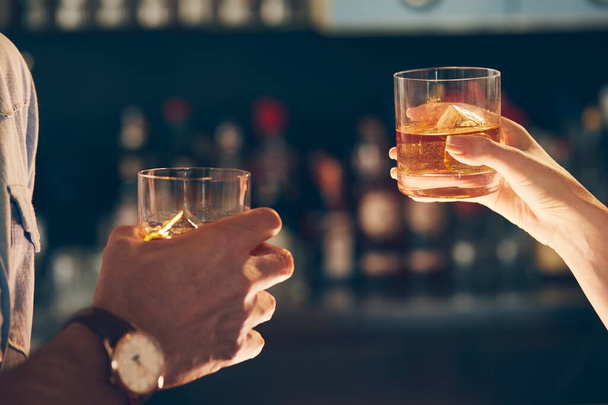 A closeup shot of two people clinking glasses with alcohol at a toast - Foto, afbeelding