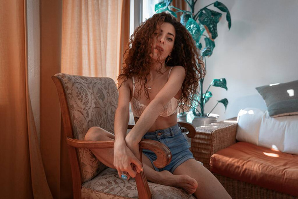 A woman with black curly hair on the armchair in a room - Fotó, kép