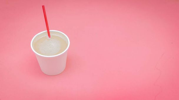 A closeup shot of a white paper cup filled with coffee with milk on a pink background - Фото, зображення