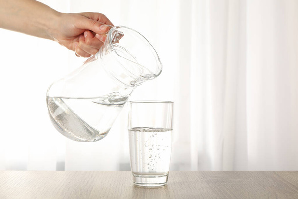 Pouring purified fresh water from the jug in glass on wooden table - Photo, Image