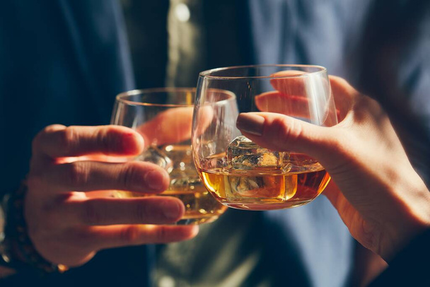 A closeup shot of two people clinking glasses with alcohol at a toast - Fotó, kép