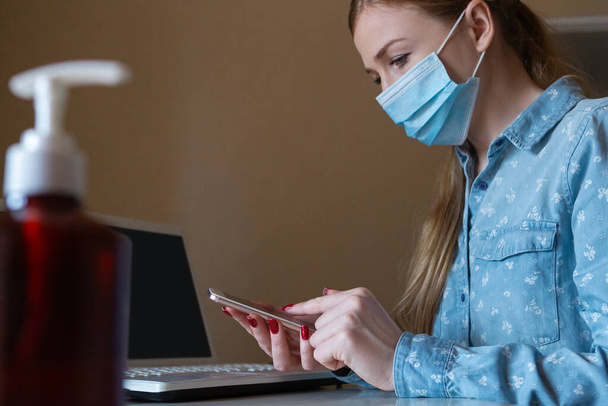 Young woman in face mask disinfecting gadgets surfaces on her workplace - Zdjęcie, obraz