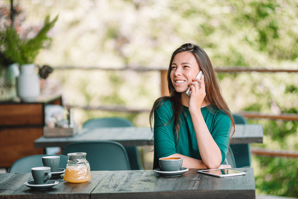 Mujer joven con teléfono inteligente mientras está sentada sola en la cafetería durante el tiempo libre
 - Foto, imagen