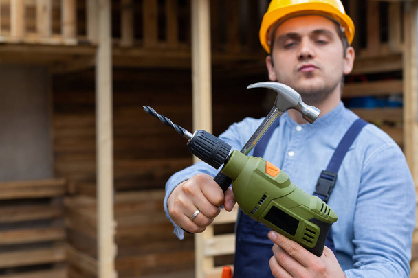 Handsome young repairman holding construction tools in front of wooden background - Photo, image