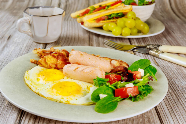 Вкусный завтрак с яйцами, сосисками, беконом, тостами и чашкой кофе
. - Фото, изображение