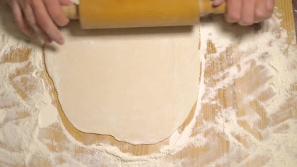 Top view, male hands roll out the dough with a rolling pin on a wooden surface, close-up. Close up of baker or chef preparing fresh dough with rolling pin on kitchen table. Male hands rolling dough. - Footage, Video