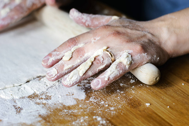 Frauenhände pflastern mit einem Nudelholz einen Teig über ein mit Mehl verschmutztes Holzbrett. Zubereitung von Lebensmitteln auf Mehlbasis wie Brot oder Pizza - Foto, Bild
