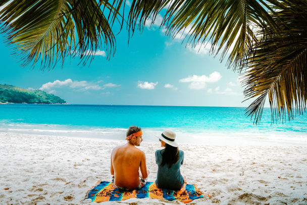 Τροπική λευκή παραλία στο νησί Praslin Σεϋχέλλες, ευτυχισμένο Νεαρό ζευγάρι άντρας και γυναίκα κατά τη διάρκεια των διακοπών Διακοπές στην παραλία χαλαρώνοντας κάτω από ένα φοίνικα - Φωτογραφία, εικόνα
