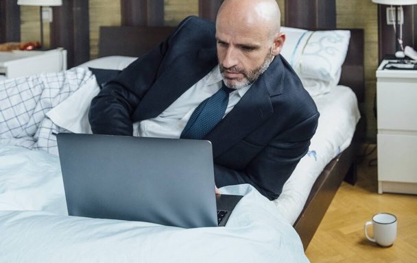 Homme d'affaires assis sur le lit avec ordinateur portable et café
 - Photo, image