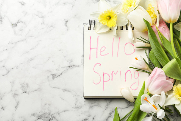 Notebook with words HELLO SPRING and fresh flowers on white marble table, flat lay. Space for text - Foto, Imagem