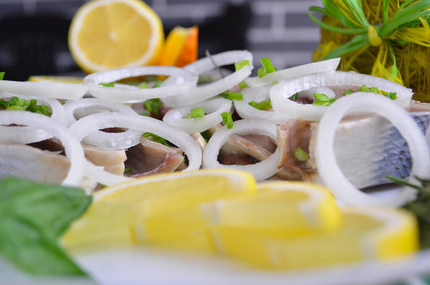 Filete de arenque con sal, pimienta, hierbas, cebolla y limón sobre un plato negro sobre fondo blanco. Vista superior. alimentos saludables
 - Foto, Imagen