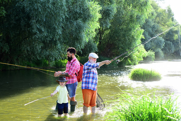 Egy kisfiú horgászik a tavon az apjával és a nagyapjával. Egy férfi a fiával és apjával a folyón horgászbotokkal. Folyami halászat. - Fotó, kép