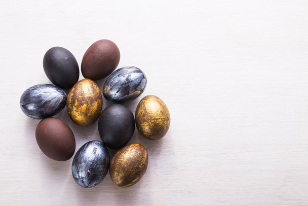 Vacaciones, tradiciones y concepto de Pascua - Huevos de Pascua con estilo oscuro sobre fondo de madera blanca con copyspace
. - Foto, Imagen
