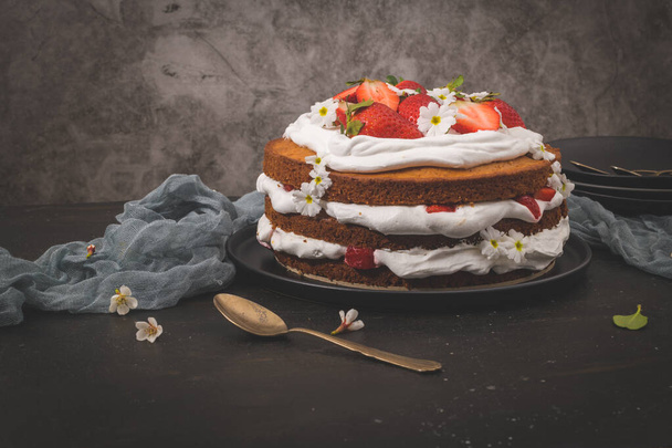 Strawberry cake, strawberry sponge cake with fresh strawberries and sour cream on a dark kitchen countertop. - Foto, afbeelding