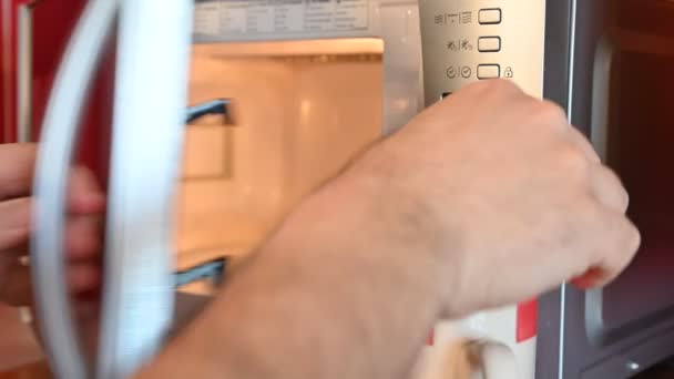 A mikrohullámú sütő használata. A fehér férfi keze betette a csészét a mikróba, aztán beállította az időzítőt, és elindította a programot.. - Felvétel, videó