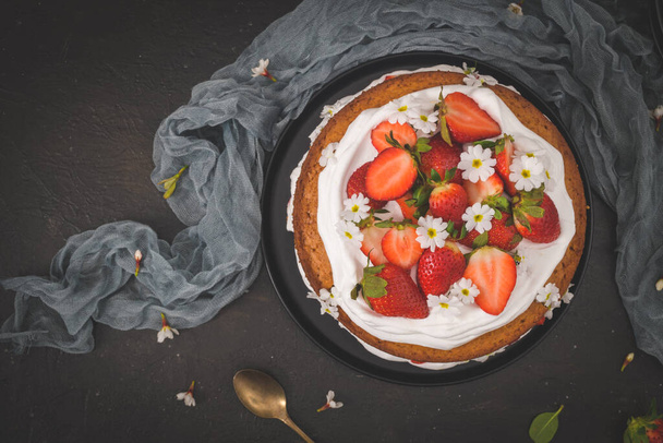 Strawberry cake, strawberry sponge cake with fresh strawberries and sour cream on a dark kitchen countertop. - Photo, Image