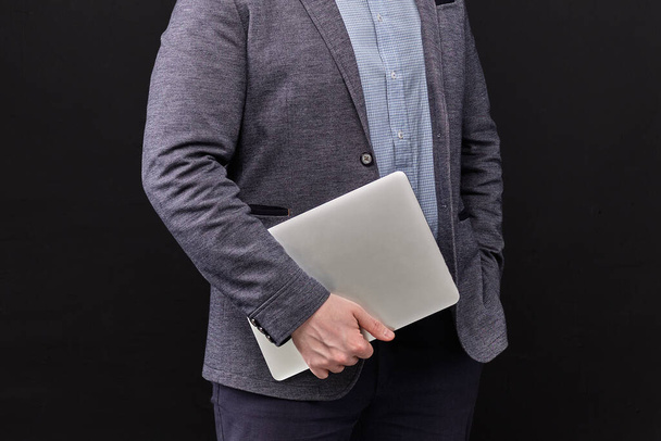 Un hombre con una chaqueta sosteniendo un portátil sobre un fondo negro. De cerca.
. - Foto, Imagen