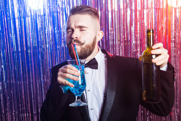 Club party and holidays concept - Πορτρέτο του κομψού όμορφου άνδρα με ακριβό κοστούμι κρατά μπλε κοκτέιλ σε λαμπερό φόντο. - Φωτογραφία, εικόνα