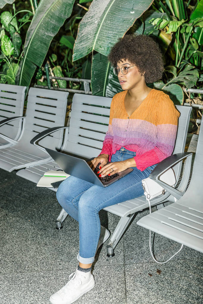 Blick auf eine Frau mit bunter Brille und Jeans, die mit ihrem Laptop an einem Bahnhof sitzt - Foto, Bild